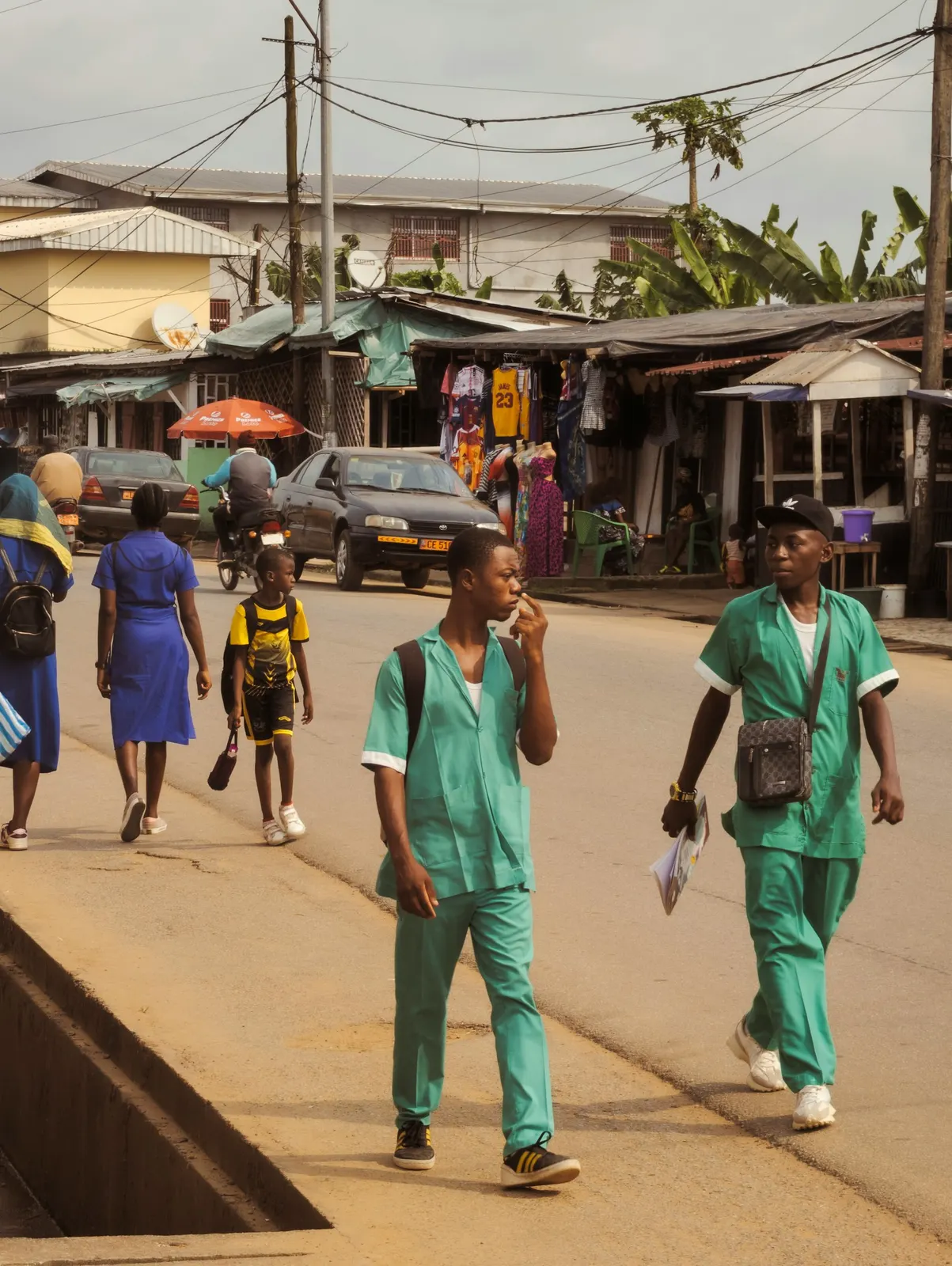 Two health workers in green scrubs walking down a busy street