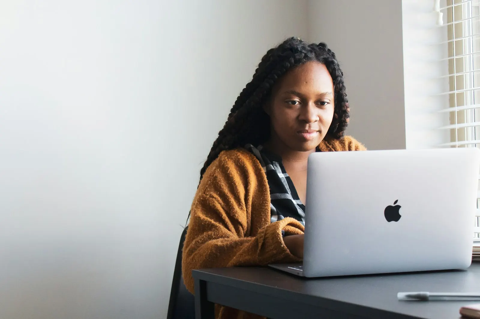 A young woman with braided hair working on a laptop at her desk