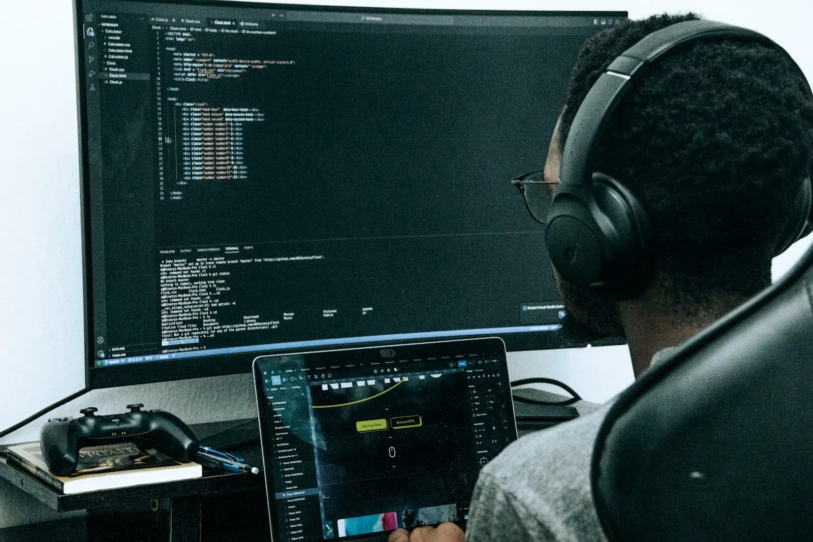 A developer in headphones working across a laptop and a large monitor of code